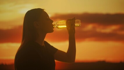 Silhouette of a Woman Drinking Water Against a Sunset Background