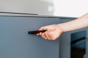 Closeup on woman hand hold black handle and open cupboard door at kitchen