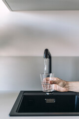 Woman filling drinking glass with clean water from under the tap