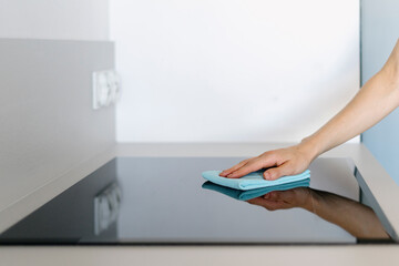 Woman using blue microfiber cloth rubs glass ceramic stove in the kitchen
