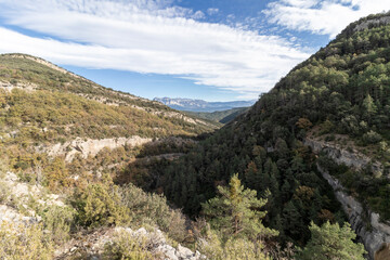 a scenic mountainous landscape, densely covered with green trees under a blue sky with wispy clouds. It’s a serene, undisturbed natural scene