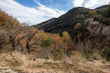 a scenic mountainous landscape with sparse dry vegetation and trees under a partly cloudy sky