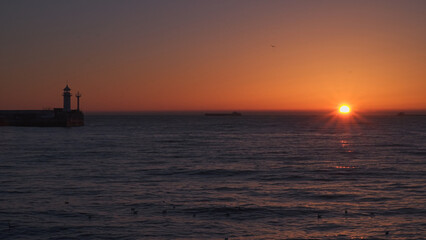 Sunrise at sea. Ships and a lighthouse can be seen on the horizon