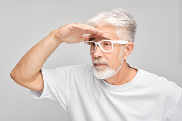 Senior man with white hair and glasses looking into the distance with hand above eyes, searching