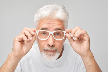 Senior man with white hair adjusting glasses looking at camera with curious expression