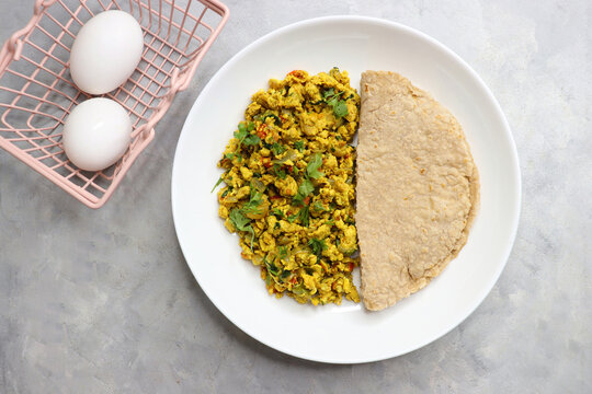 Anda Masala Bhurji or Spicy Indian scrambled eggs with jowar roti, a popular street food in Mumbai. Served in a white plate along with copy space. egg bhurji or parasi akuri. with bhakri or pav.