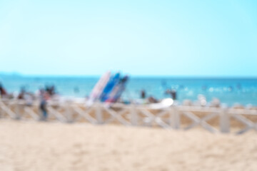 Blurred sandy beach with blue sea and resting people on summer day. Abstract bokeh background of...