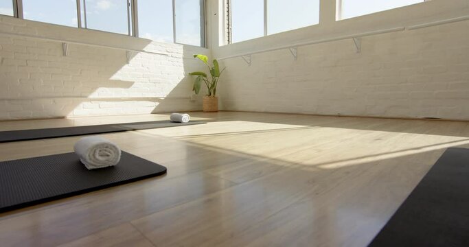 Three yoga mats are neatly arranged on a wooden floor in a bright room with large windows, with copy