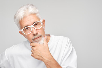 Mature man with white hair and glasses looking thoughtful against a gray background.
