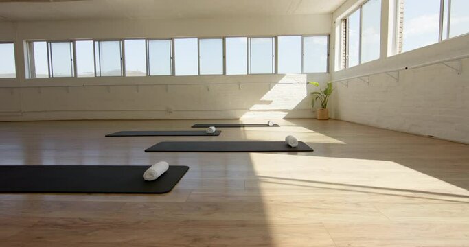 A yoga studio is bathed in natural light, with mats and bolsters neatly arranged, with copy space