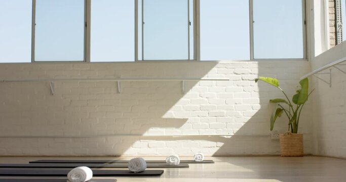 Sunlight streams through large windows onto yoga mats in a serene studio with copy space