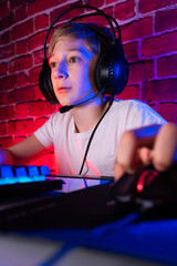 A keen fellow gamer in front of a computer. A gamer boy plays computer games against a neon lit brick wall. © Roman