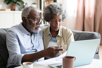 Senior couple checking and calculate financial billing together on sofa. Mature couple discussing their monthly expenses at home. Elderly couple keeping an eye on their finances. 