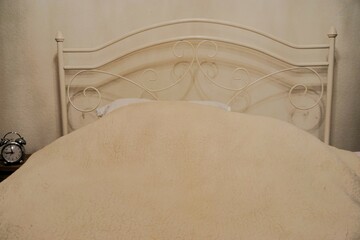 Bett mit weißem Metallgitter vor weißer wand und weißer Schafwolldecke in Schlafzimmer