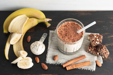 Glass with protein drink, healthy milkshake smoothie on wooden board with bananas, protein powder...