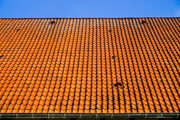 Großes langes orangenes Ziegeldach von Gebäude vor hellblauem Himmel bei Sonne am Morgen im Frühling