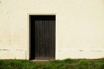 Beige Betonfassade von altem sanierten Stallgebäude mit brauner alter Holztür bei Sonne am...