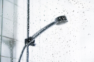 Shower and water on glass screen. Cabin stall window with drops in focus. Faucet head in bathroom. ...