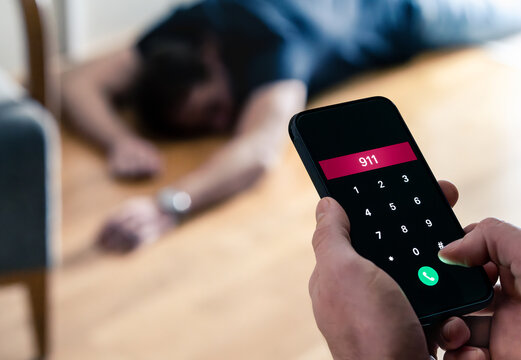 Emergency call 911. Accident or epilepsy. Unconscious fainted young man lying on the floor. SOS ambulance alarm with phone in hand. Urgent medical help aid. Alcohol poisoning or overdose at a party.