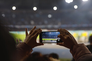 A spectator captures the intense atmosphere of a nighttime sports event, the stadium lights...