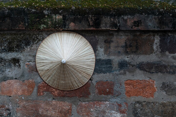 Traditional Vietnamese conical straw hat hanging on a brick wall