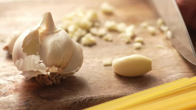 Chopping garlic on a cutting board with pasta. Fried Assassin's Spaghetti Cooking Step. Close-up, shallow dof.