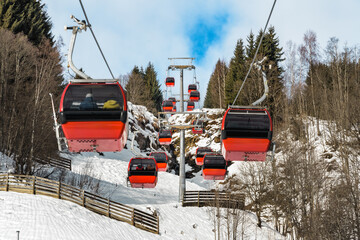 Red gondola lifts on a snowy mountain with pine trees and blue sky, gondola cableway. Perfect for winter sports, travel, and nature themes