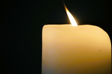 Dicke weiße Kerze mit flackerndem Kerzenlicht vor schwarzem Hintergrund 