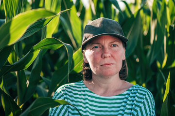 Female farmer and agronomist posing in green corn crop agricultural field and looking into distance...