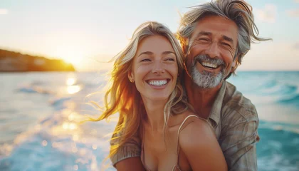 Rolgordijnen zonder boren Strand zonsondergang  Laughing Middle-aged Couple in love portrait while walking by sandy ocean beach in evening sunset hours on seashore on exotic island. People relationship and tropic honeymoon vacations concept photo.