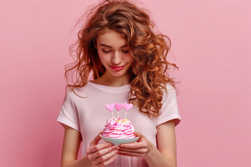 Girl with cupcake in hands and burning candles, birthday on pink background
