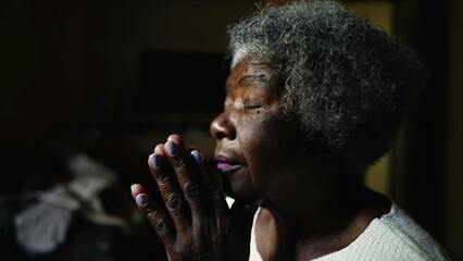 Devout Christian Senior African American woman in PRAYER at home, close-up face of one black...