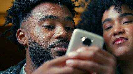 African American young couple close-up faces staring at cellphone device in foreground. People...