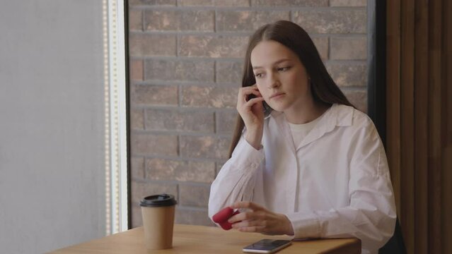 In cafe young girl takes out earbuds from case plugs into ears listening music. Coffee cup nearby girl enjoys blend of favorite music in earbuds and aroma of cup of coffee Listening music in earbuds