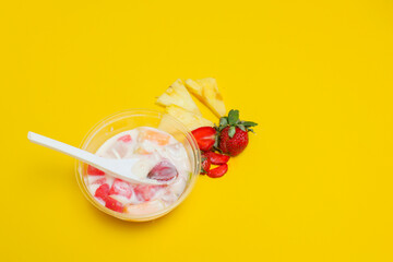 es buah or sup buah is indonesian fruit cocktail ice desert, contains strawberry, pineapple, and other tropical fruits mixed with ice cube, and condensed milk. isolated on yellow background.