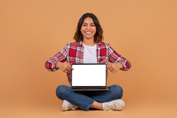 Happy middle eastern woman sit on floor, point at laptop