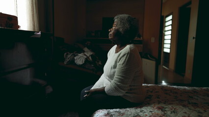 Lonely South American elderly lady sitting by bedside with peace tranquil gaze at window inside...