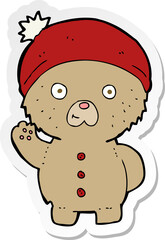 sticker of a cartoon waving teddy bear in winter hat