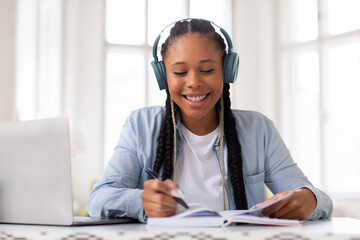 Happy black female student studying with headphones and laptop - obrazy, fototapety, plakaty