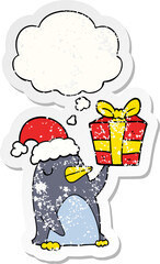 cartoon penguin with christmas present and thought bubble as a distressed worn sticker