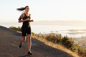 Athlete, woman and running in road with music for sport, exercise or fitness for competition or marathon in nature. Runner, person and workout with wellness, seaside or earphones for cardio in Mexico
