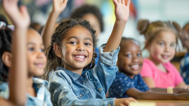Primary school diverse cheerful smiling children sitting in light classroom with their hands up eager to answer the teacher's question