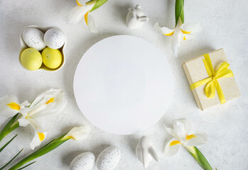 Fototapeta na wymiar Easter layout. Decorative eggs, iris flowers, gift box, bunnies around round blank space on white.