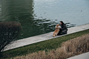 Charming red fluffy Welsh corgi Pembroke is like a fox. A young pretty Caucasian woman walks with her dog along the Sava River embankment in Belgrade.