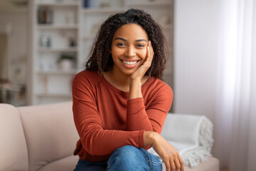 Portrait of attractive black woman with captivating smile sitting casually on sofa