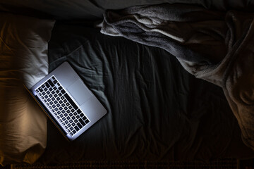 Laptop on the bed at night, light from the laptop screen, top view.