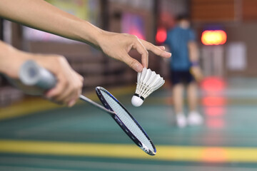 Badminton player holds racket and white cream shuttlecock in front of the net before serving it to another side of the court, soft focus. - obrazy, fototapety, plakaty