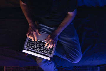 Busy man networking on laptop late at night, typing text, working overtime.