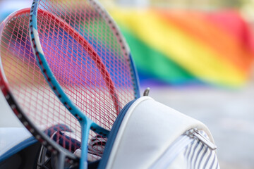 Badminton sport equipments, rackets and sportbag placed on floor with blurred rainbow flag background, concept for popular sports with all gender and lgbt people around the world. - obrazy, fototapety, plakaty