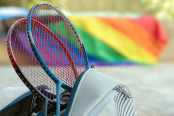 Obraz premium Badminton sport equipments, rackets and sportbag placed on floor with blurred rainbow flag background, concept for popular sports with all gender and lgbt people around the world.